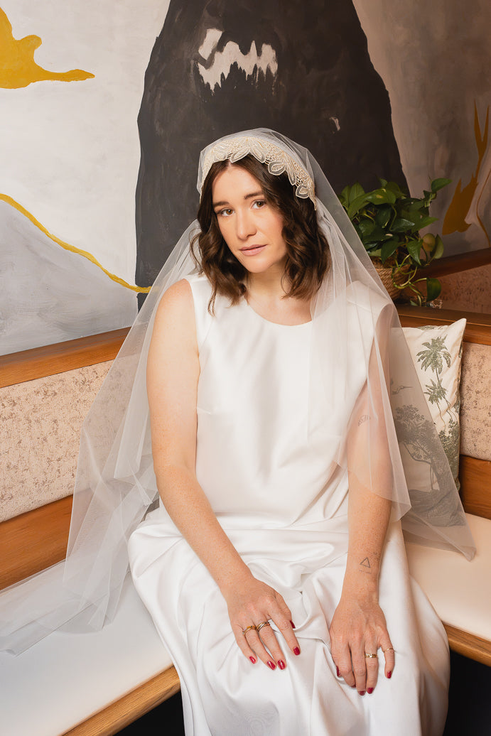 Sitzende Braut mit Juliet-Cap-Schleier MAHINA und handbestickter Spitzenkante in Champagner
