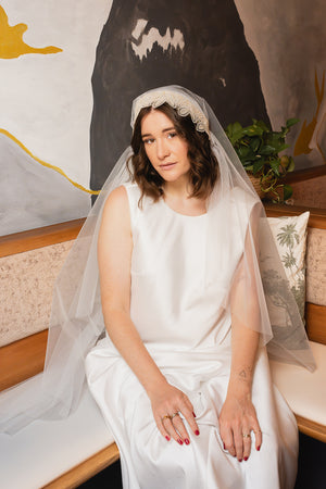 Sitzende Braut mit Juliet-Cap-Schleier MAHINA und handbestickter Spitzenkante in Champagner