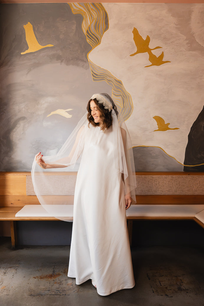 Sitzende Braut mit Juliet-Cap-Schleier MAHINA und handbestickter Spitzenkante in Champagner