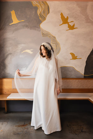 Braut hält den Tüll des Juliet-Cap-Schleiers MAHINA lächelnd zur Seite